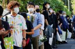A queue of mourners outside the funeral venue holding flowers and other tributes