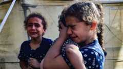 A girl of about seven hugs a toddler, crying. Another young girl sobs behind them