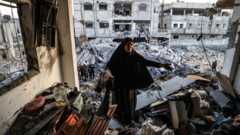 A woman inspects a destroyed building in Rafah, Gaza