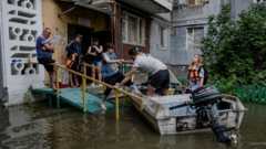 Οι κάτοικοι απομακρύνονται από το κτήριο τους σε μια πλημμυρισμένη περιοχή της Χερσώνας,