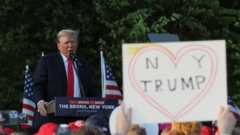 Donald Trump speaks at a campaign rally in The Bronx, New York; in the foreground, a supporter holds up a sign reading: "NY (heart) Trump"