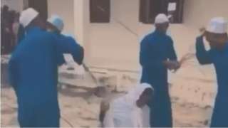 Screenshot from the video showing two pupils receive severe beatings. One student is kneeling. The other is lying flat on the ground.