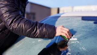 A person scraping ice off their car windshield