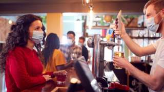 Barman in a mask serving customer in a pub