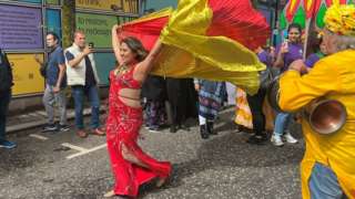 A dancer holding up red and yellow fabric during the Mela parade