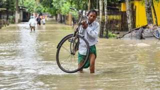A man carries his bicycle as he wades through flood waters in Solmara of Nalbari district, in India's Assam state on June 19, 2022