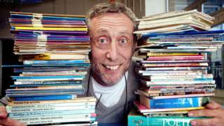 Michael Rosen flanked by piles of books