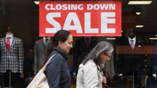 People walk past closing down sign in shop window.