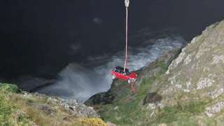 Car being lifted by crane from bottom of cliff