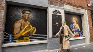 A woman walks past a mural in Belfast showing Sunak and Truss as boxers, fighting for No 10