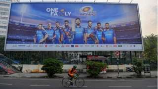 In this picture taken on October 10, 2020, a cyclist rides past a hoarding of Mumbai Indians cricketers of the Indian Premier League (IPL) cricket tournament in Mumbai.