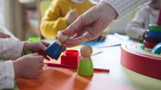 Stock photo shows an adult hand passing a toy to the hand of a young child