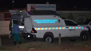 Members of the Forensic Pathology Services stand near their vehicles on the scene of a mass shooting in Gqeberha,