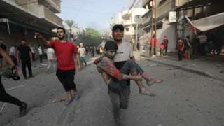 A Palestinian man carries a wounded boy following an Israeli air strike in northern Gaza (28 October 2023)