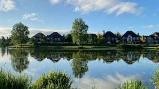 Houses, trees and clouds reflected in still water
