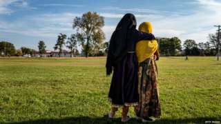Two Afghan women embrace in a field at Fort McCoy, Wisconsin