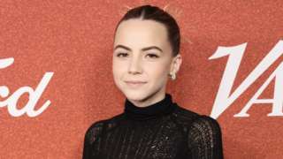 Bobbi Althoff attends Variety Power of Young Hollywood at NeueHouse Los Angeles on August 10, 2023 in Hollywood. Bobbi, a white woman in her 20s, wears a high-necked black dress. She has her brunette hair tied back in a tight bun and has blacked winged eyeliner highlighting her hazel brown eyes. She otherwise wears very light make-up with a pale pink lipstick. She wears no jewellery with the exception of small silver hoop earrings.