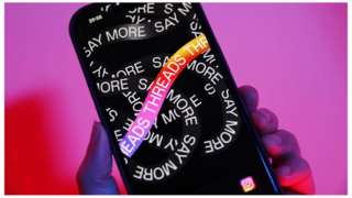 A hand holding a phone with the Threads logo on it.