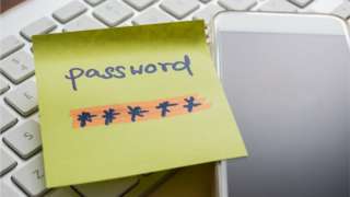 A password on a post-it note next to a keyboard and phone