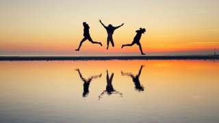 Three children jumping on West Wittering beach in West Sussex