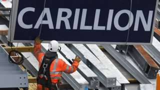 A construction worker guides down a sign showing the name of Carillion
