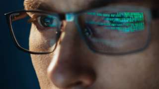 A stock image of someone looking at a screen with code reflected in their glasses