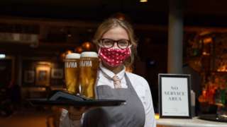 A waitress wearing a mask carried a tray of beers