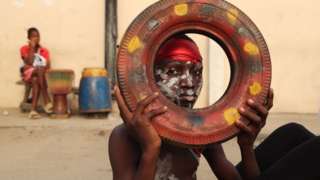 A boy with face paint hold up a tyre with multicoloured paint on it.