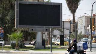 Vehicles drive past an advertisement screen at the Uqba Bin Nafia square in Baghdad