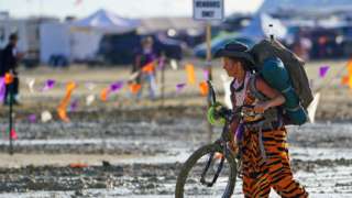 A Burning Man participant walks their bike through the mud