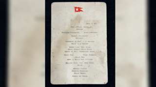 First-Class menu from the Titanic. It has water stains on it and a red emblem of a flag at the top.