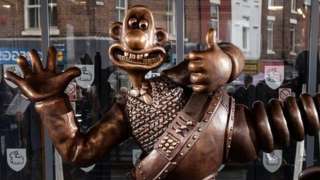 Nick Park poses on bench with Wallace and Gromit statue