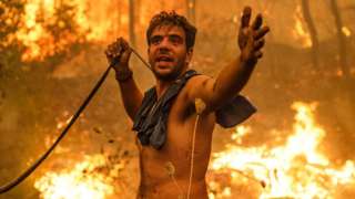 A local resident gestures as he holds an empty water hose during an attempt to extinguish forest fires approaching the village of Pefki on Evia island, Greece, on 8 August 2021