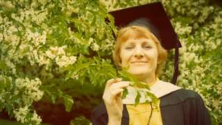 Dorothy Miles in a flowering tree, wearing a graduation gown and cap