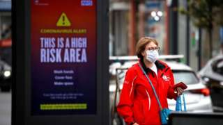 A woman wearing a protective mask walks past a warning sign in Greater Manchester