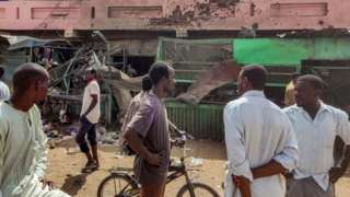 People walk past a building riddled with bullet holes at a market hit by shelling in the south of Khartoum - Thursday 1 June 2023