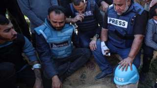 Wael al-Dahdouh places a blue "press" helmet on the grave of his son, Hamza al-Dahdouh, after he was killed in an Israeli air strike in Rafah, in the southern Gaza Strip (7 January 2024)