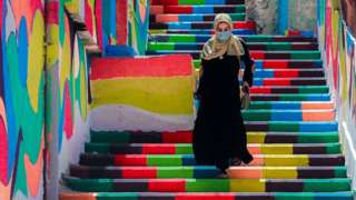 A woman, wearing a protective mask, walks down steps decorated with vibrant colours in Gaza City, on 3 May 2021