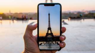 The Eiffel Tower on a smartphone camera screen, with the real Eiffel Tower in the background