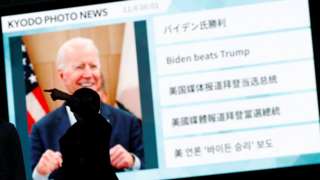 Passersby are silhouetted against a big screen showing reports on Joe Biden"s U.S. presidential election victory in Tokyo