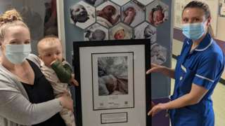 Ali Harris holding baby Indy while handing over a framed photo to a nurse