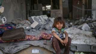 A Palestinian child sits in the rubble of their home