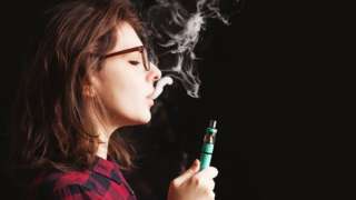 Young woman wearing glasses and smoking an e-cigarette.