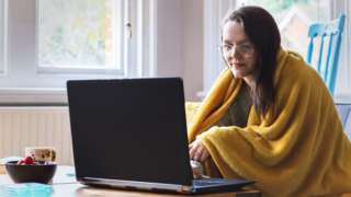 Woman home-working with a blanket over her shoulders