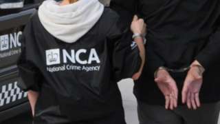 An NCA officer leads a person away in handcuffs
