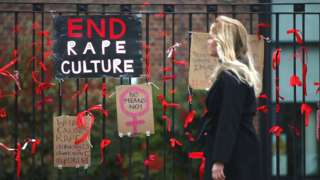 A woman walks past a placard saying 'End Rape Culture'