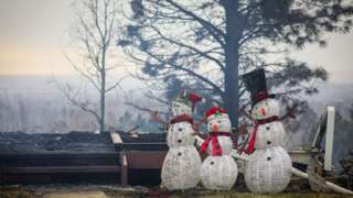 Fake snowmen stand beside burnt out homes