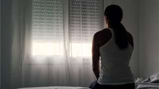Stock photo of an abused woman sitting on her bed looking out the window