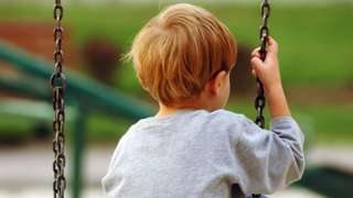 Stock image of an anonymous boy sat on a swing outdoors