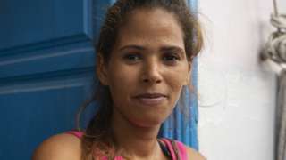 A woman dressed in pink stands leaned against a blue door